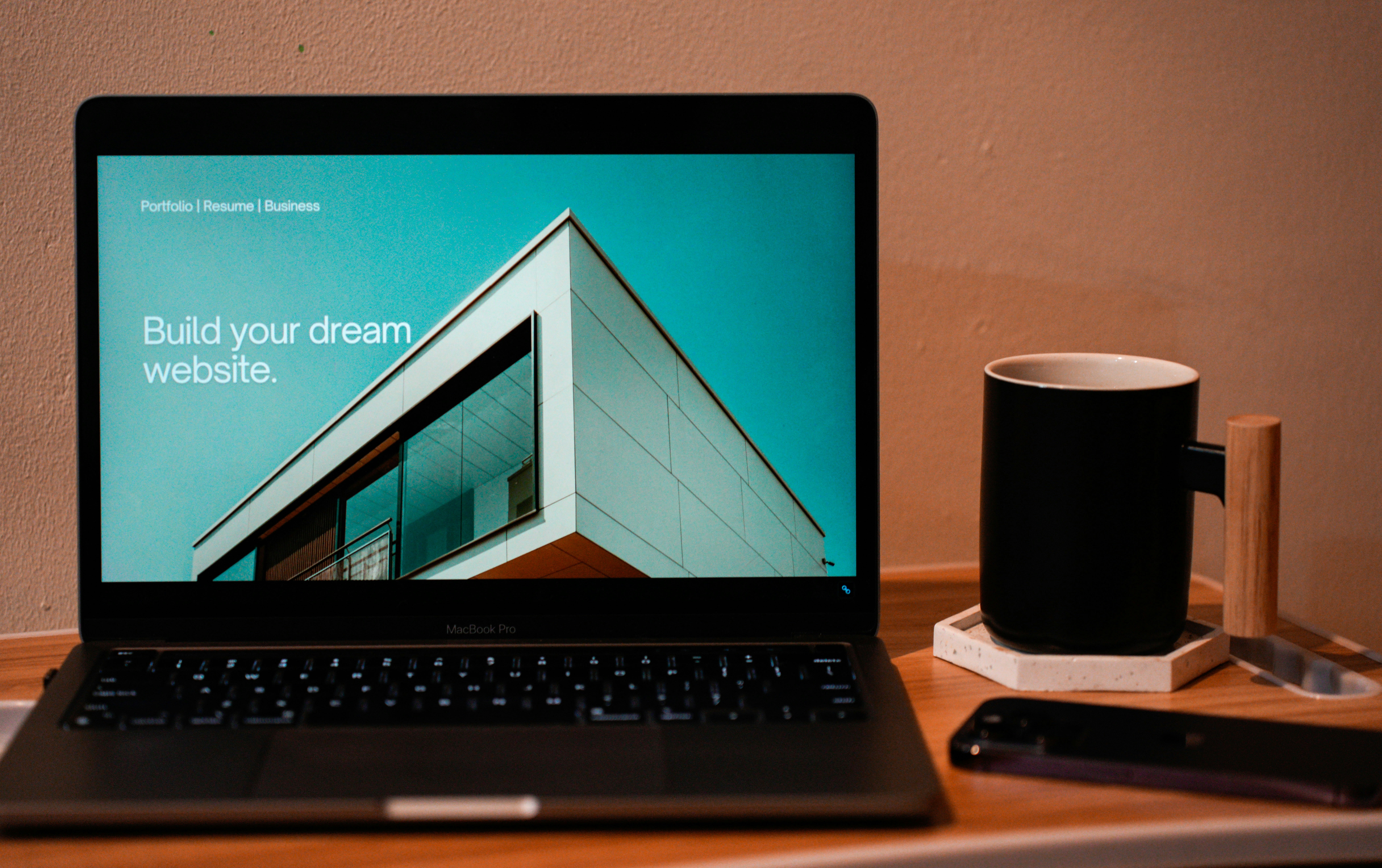Laptop displaying a responsive website homepage featuring modern architectural design and the phrase "Build your dream website." The setup includes a smartphone and coffee mug on a wooden desk, representing a UX-focused digital workspace optimized for e-commerce design and development.